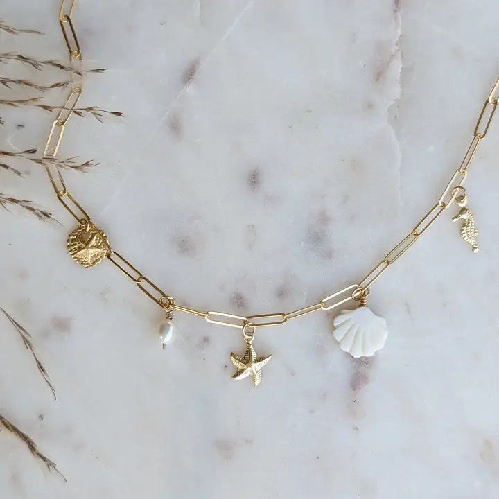a gold paperclip chain with 14k gold fill charms of a seahorse, sand dollar, starfish, mother of pearl shell, and freshwater pearls