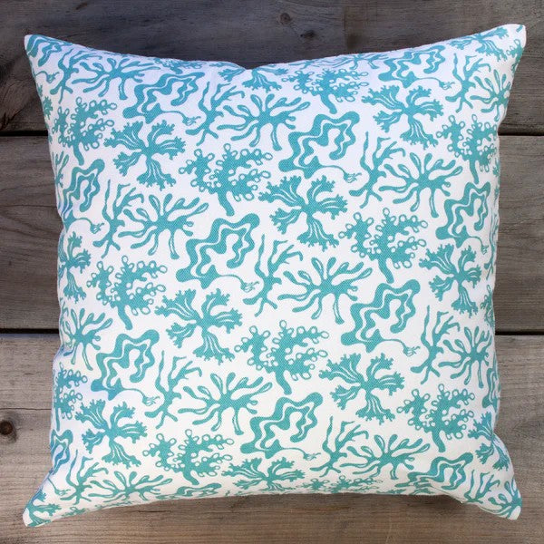 Decorative pillow with teal seaweed pattern on a wooden surface