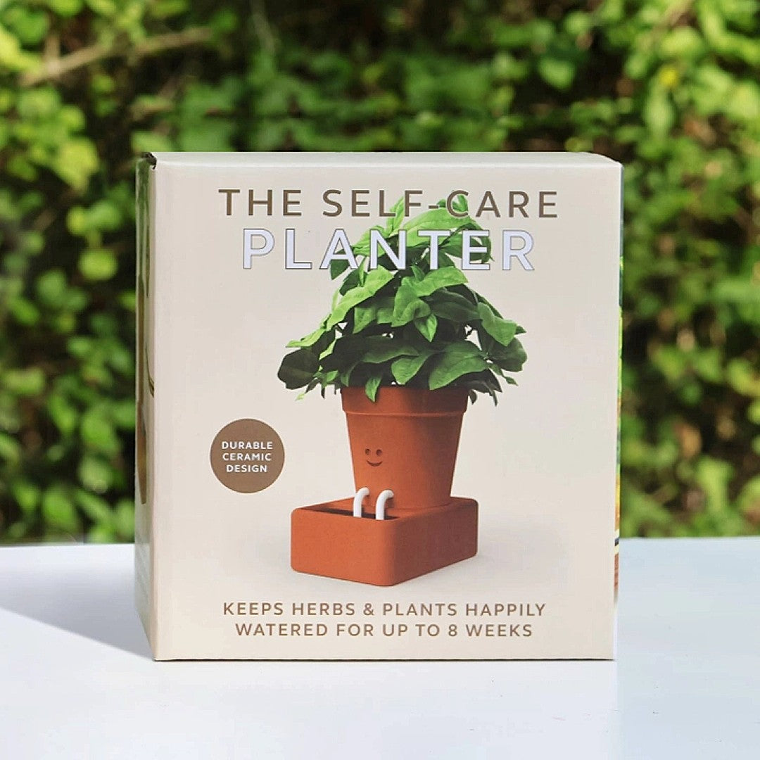Box of 'The Self-Care Planter' with a smiling ceramic planter on a white surface with greenery in the background.