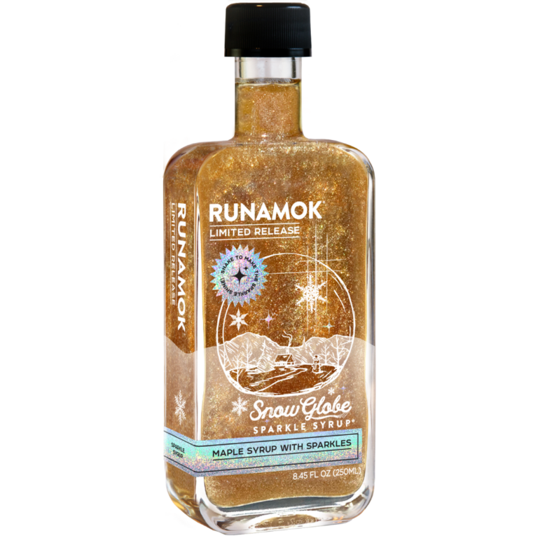 snow globe sparkle syrup bottle showing the charming winter themed label featuring a round globe with a snowy landscape with a cozy cabin surrounded by trees and snowflakes