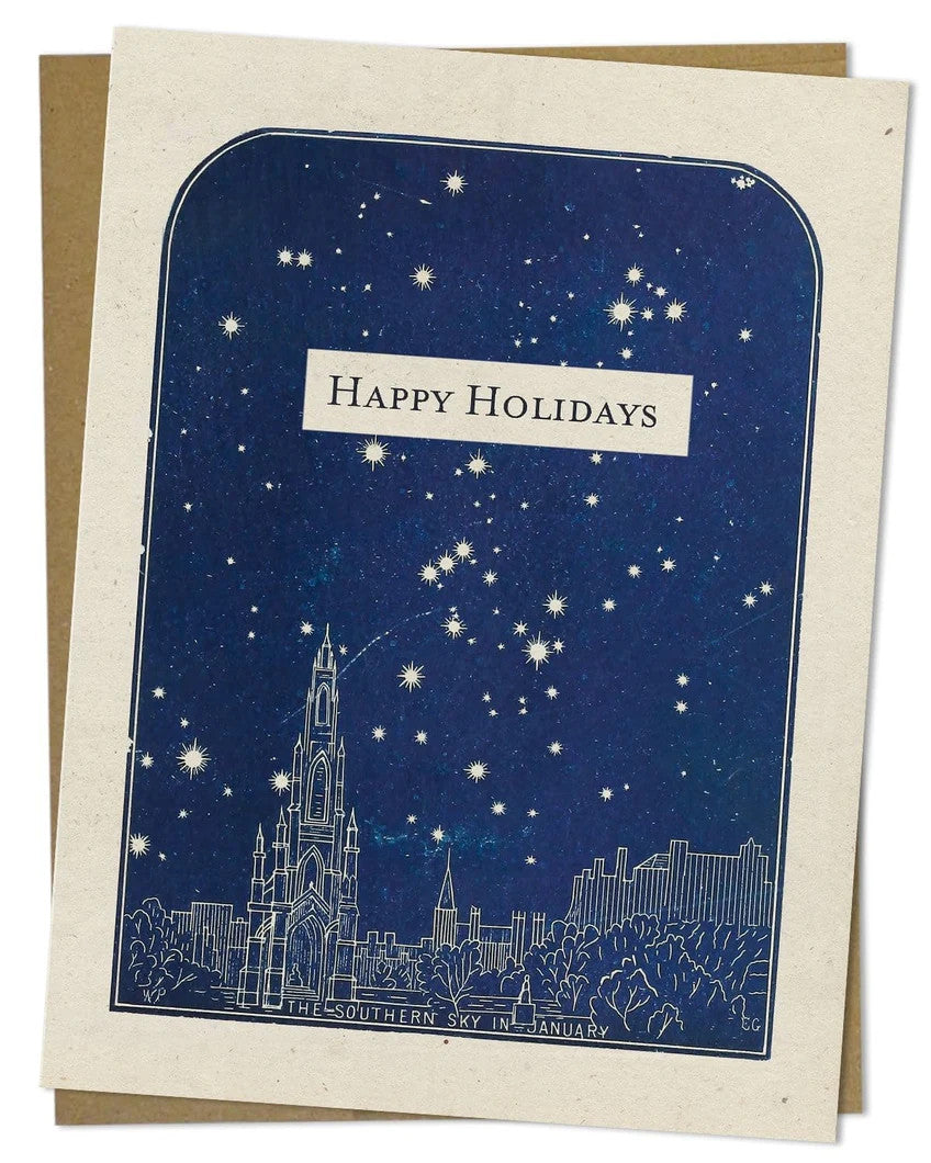 a close up look of the details of an off white greeting card that reads "Happy Holidays" with a vintage illustration of a city with a navy blue sky of stars shining above it, the bottom of the plate reads "southern sky in january"