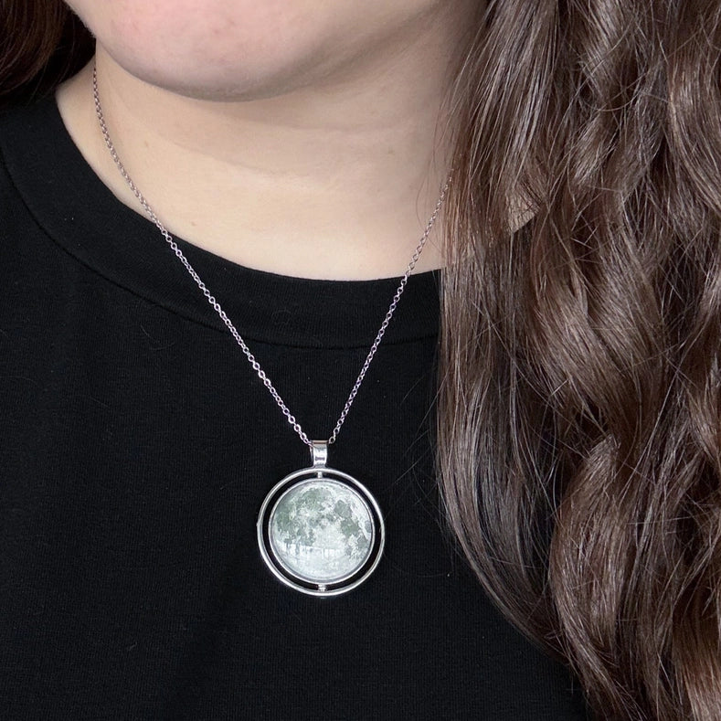 Person wearing a necklace with a moon-phase pendant on a black shirt