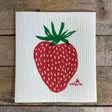 a white, rectangular dish cloth with a large hand printed strawberry illustration in red and green