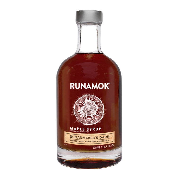 a clear glass bottle filled with dark amber colored maple syrup with an elegant label that reads "Runamok Maple Syrup Sugarmaker's Dark" with a graphic of a cross section of a maple tree