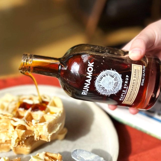 a close up of a bottle of Sugarmaker's Dark maple syrup being poured onto a stack of waffles