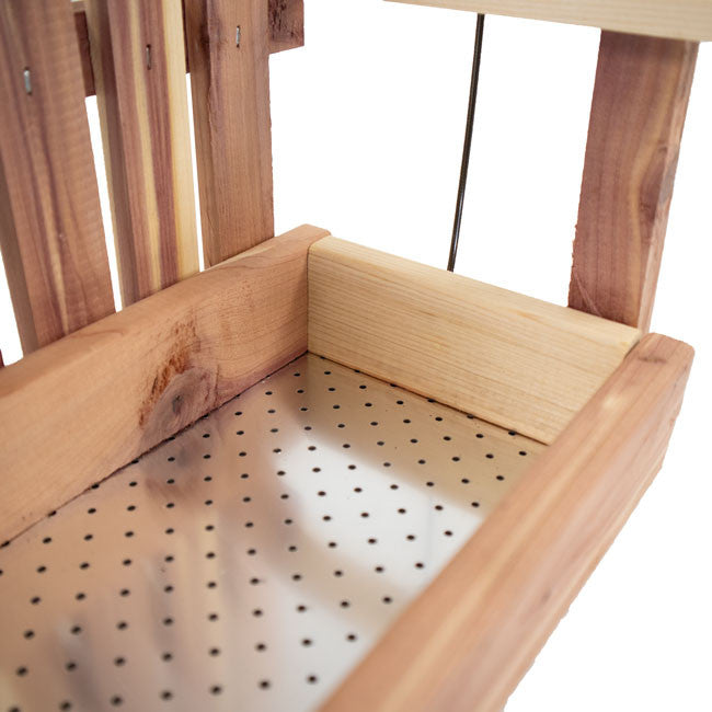 a close up view of the seat of the cedar swing bird feeder showing the empty seat of the swing with metal perforated base to keep seed aerated