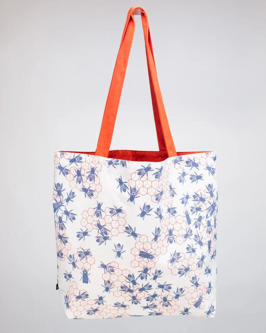 side two of the bee hive tote - a white tote bag with orange straps with a repeated orange honeycomb design that is adorned with blue bees