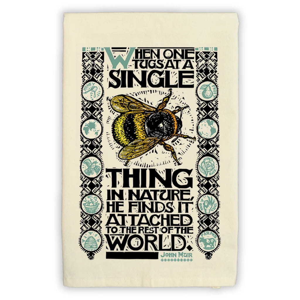 a folded tea towel featuring an illustration of a bee with the John Muir quote, "When one tugs at a single thing in nature, he finds it attached to the rest of the world"