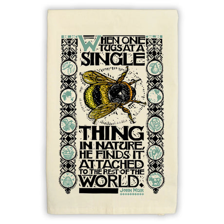 a folded tea towel featuring an illustration of a bee with the John Muir quote, "When one tugs at a single thing in nature, he finds it attached to the rest of the world"