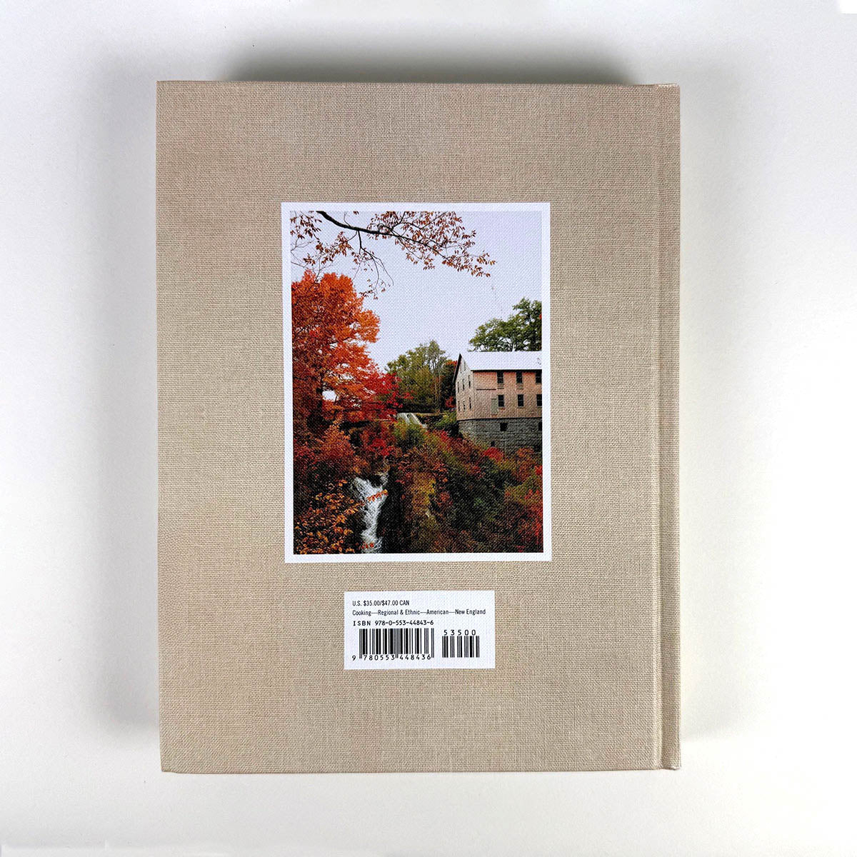 Beige book with a postcard featuring a scenic view of trees and a building on a white background