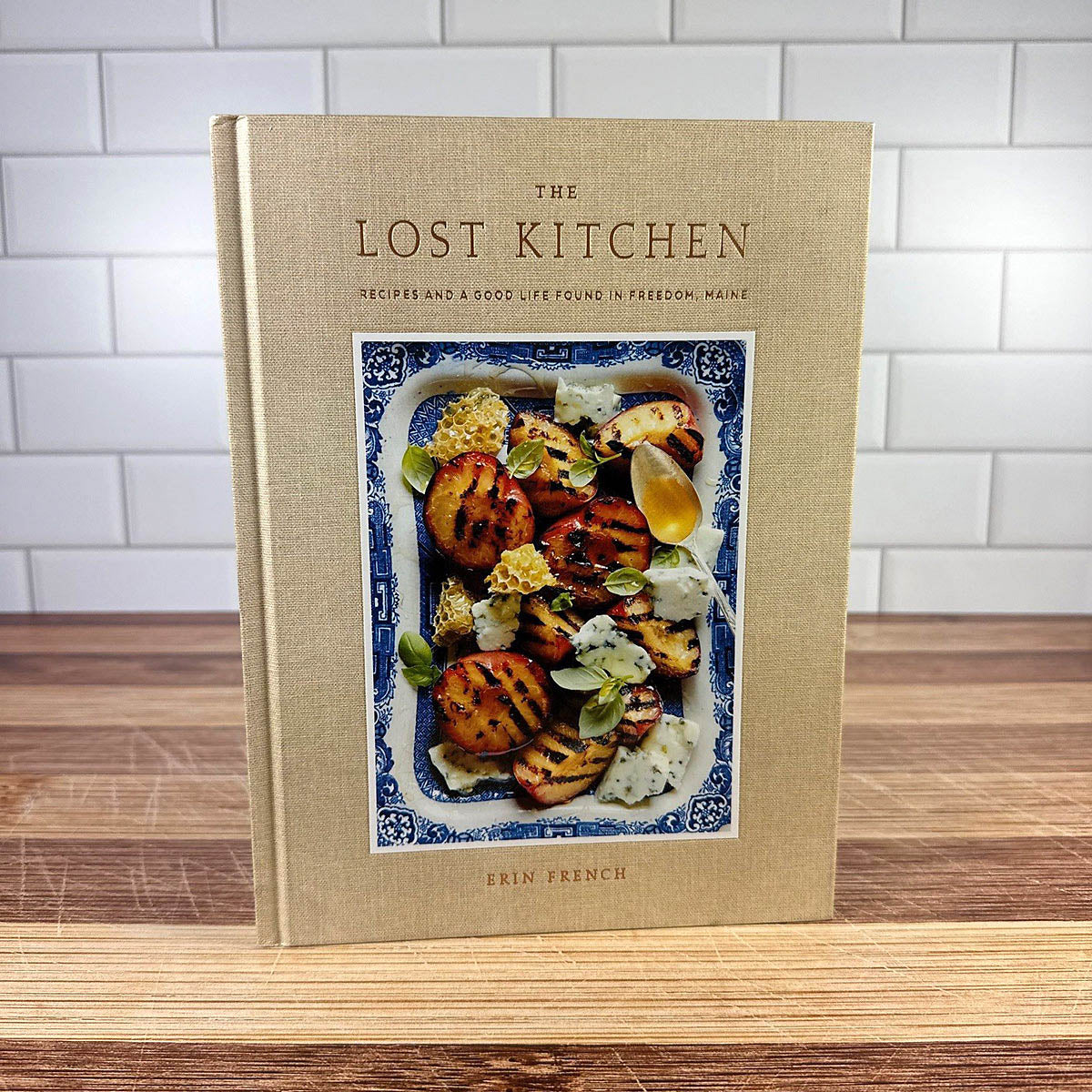Cookbook titled 'The Lost Kitchen' on a wooden surface with a tiled wall background