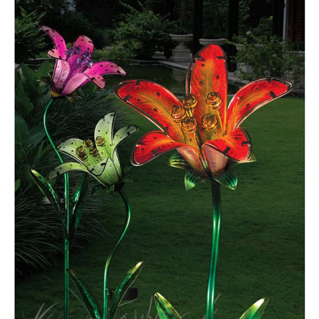 a pink, white, and red tiger lily solar stake illuminated in a garden at night