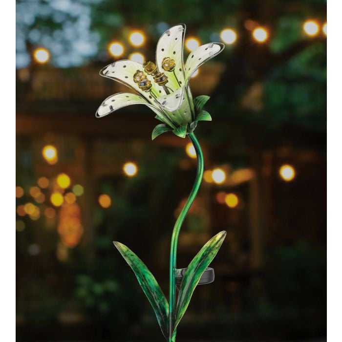 the white tiger lily solar stake illuminated in a garden at night