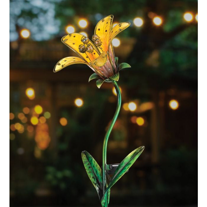 the yellow tiger lily solar stake illuminated in a garden at night