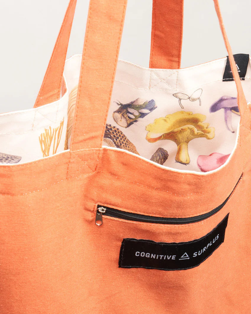 a close up of the tote near the handles showing the bag reversed so the mushroom print is on the inside of the tote and the outside is now a tangerine orange