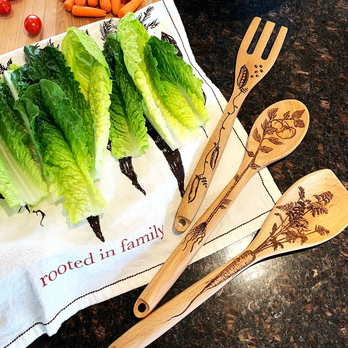 Wooden utensils with engraved designs on a kitchen towel with 'rooted in family' text.