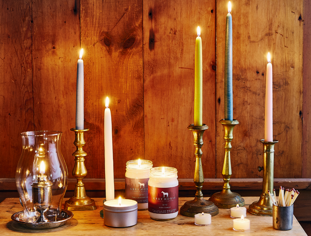 a tabletop filled with various candlesticks, oil lamps, tea light candles, and jar candles all giving off a warm glow