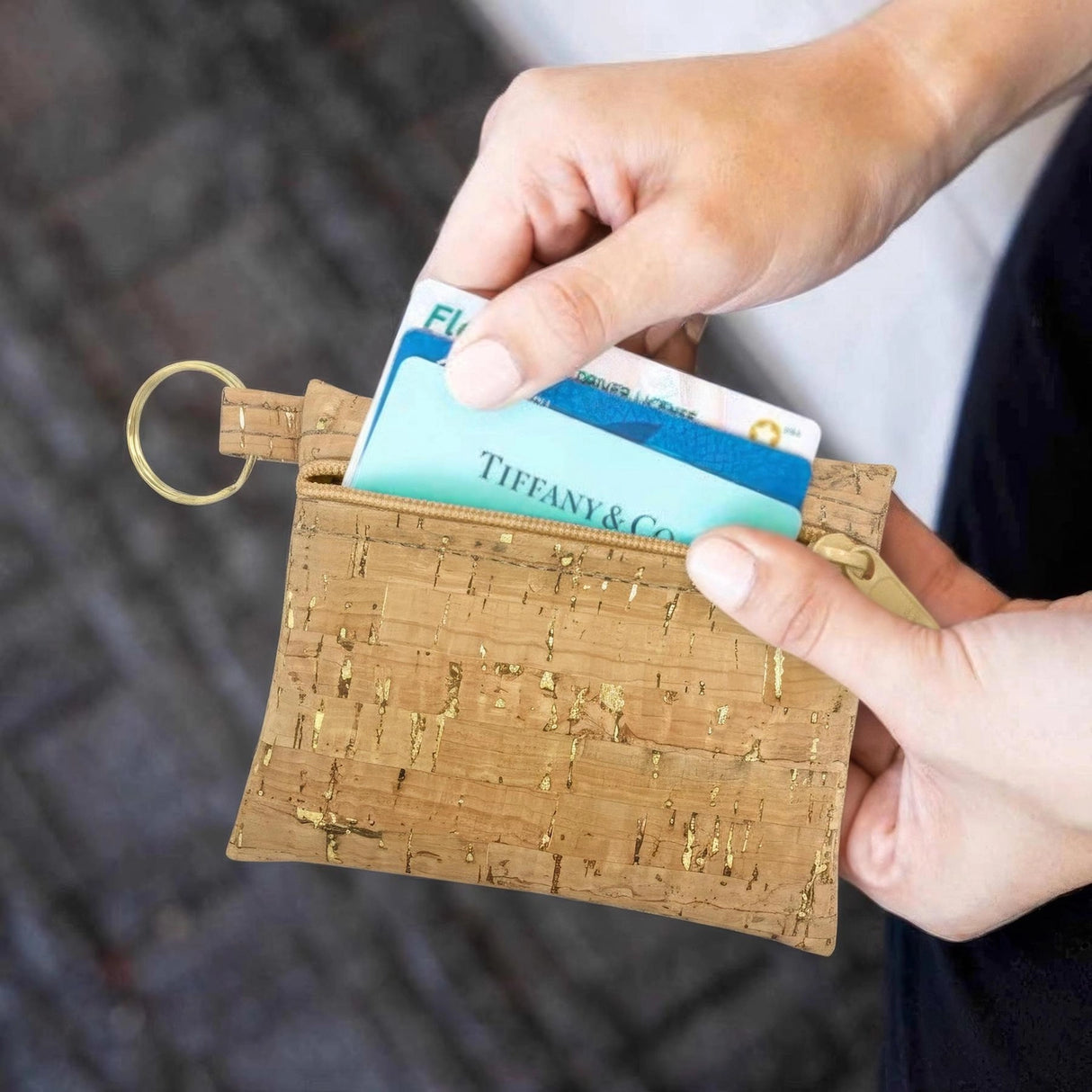 Person holding a cork keychain wallet with cards, blurred background