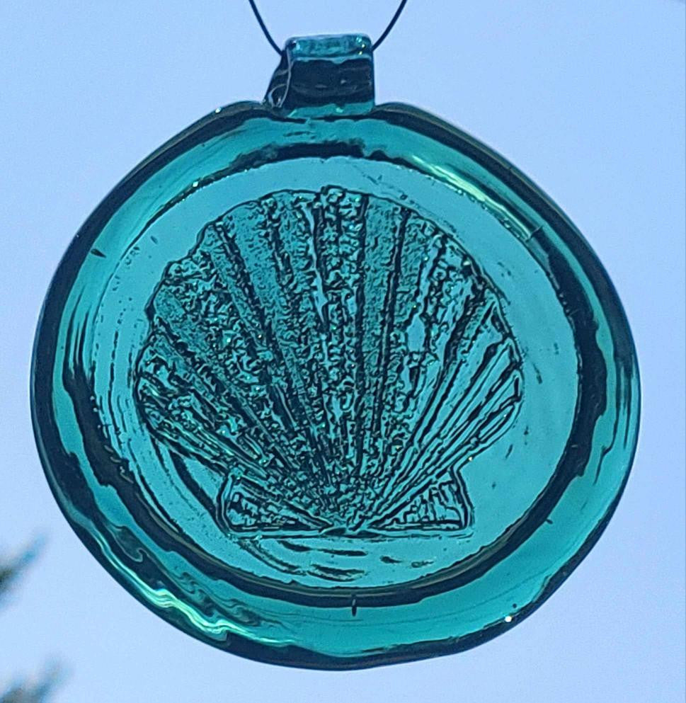 Blue glass ornament with shell design against a clear blue background