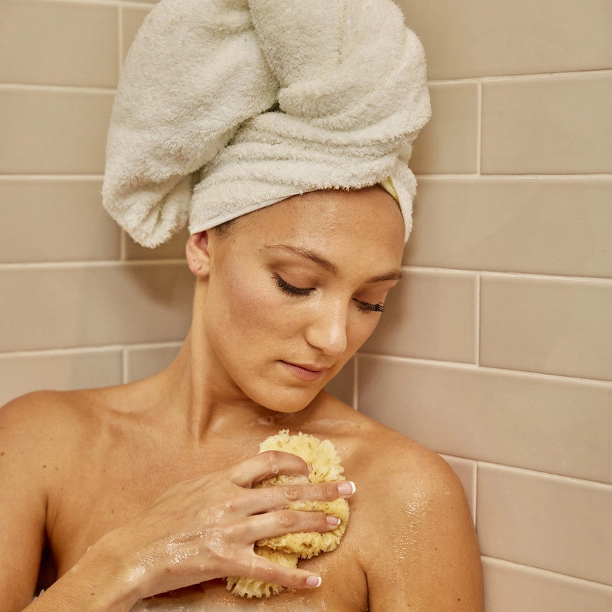 a woman in the shower bathing her skin with the wool sea sponge