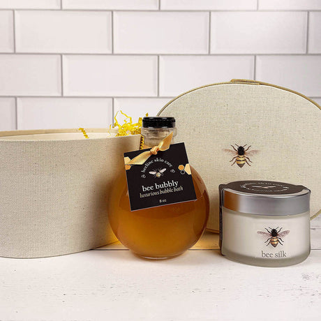 the Bee Bubbly and Bee Silk posed in front of the Beekeeper hat box on a white wood surface with white tiled background