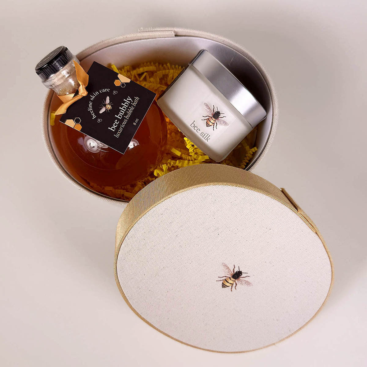 an above view of the Beekeeper's Self care box with the bubble bath and Bee Silk creme resting in the hat box with yellow crinkle paper with the top of the hat box off to the side revealing the contents