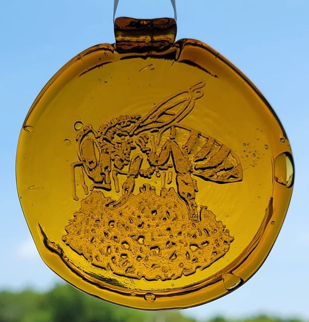 yellow glass suncatcher with bee design against a blue sky.