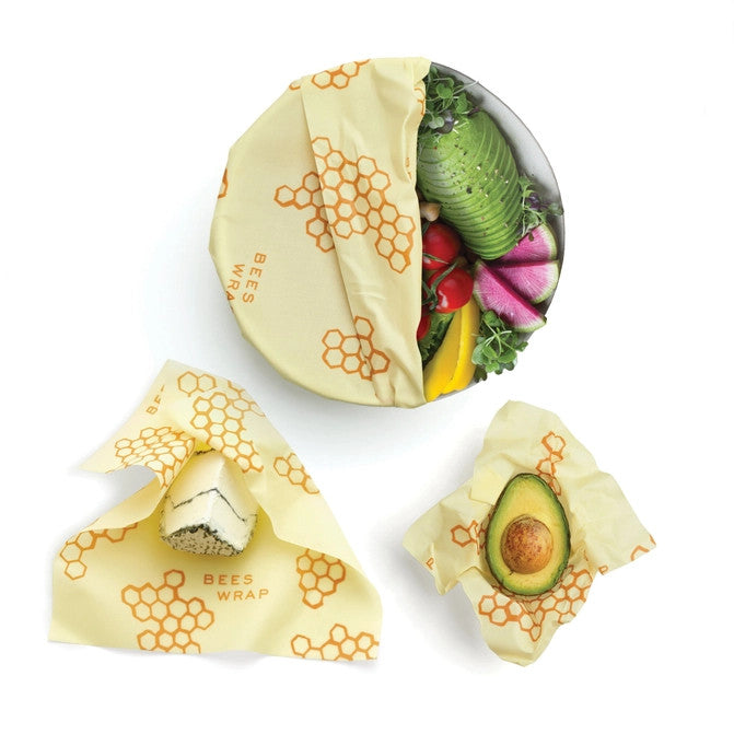 3 pieces of bees wrap in use: partially covering a salad bowl, wrapped around half an avocado, partially wrapping cheese