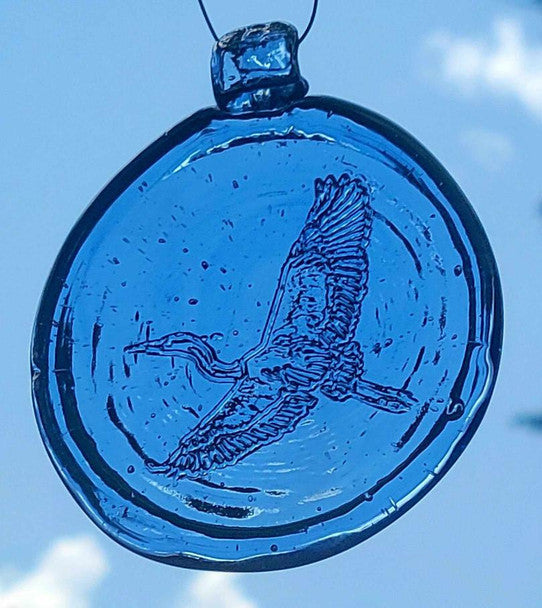 a light blue, round glass suncatcher with a relief image of a heron