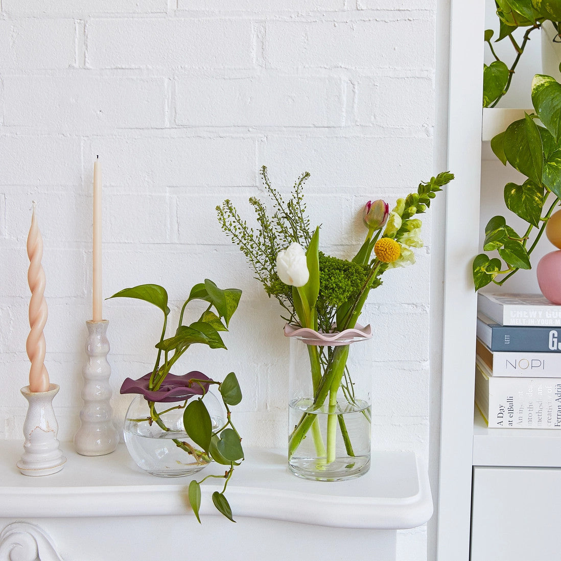 a white room with two vases filled with flowers using the botanical keepers to aid in the flower arrangement on a white mantle