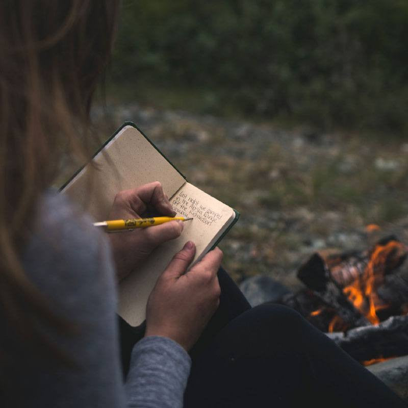 a closeup of a woman by a fire writing in her notebook