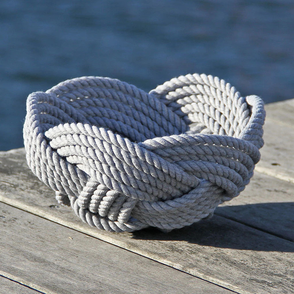 a hand woven cotton rope bowl in gray resting on a dock with a view of the water