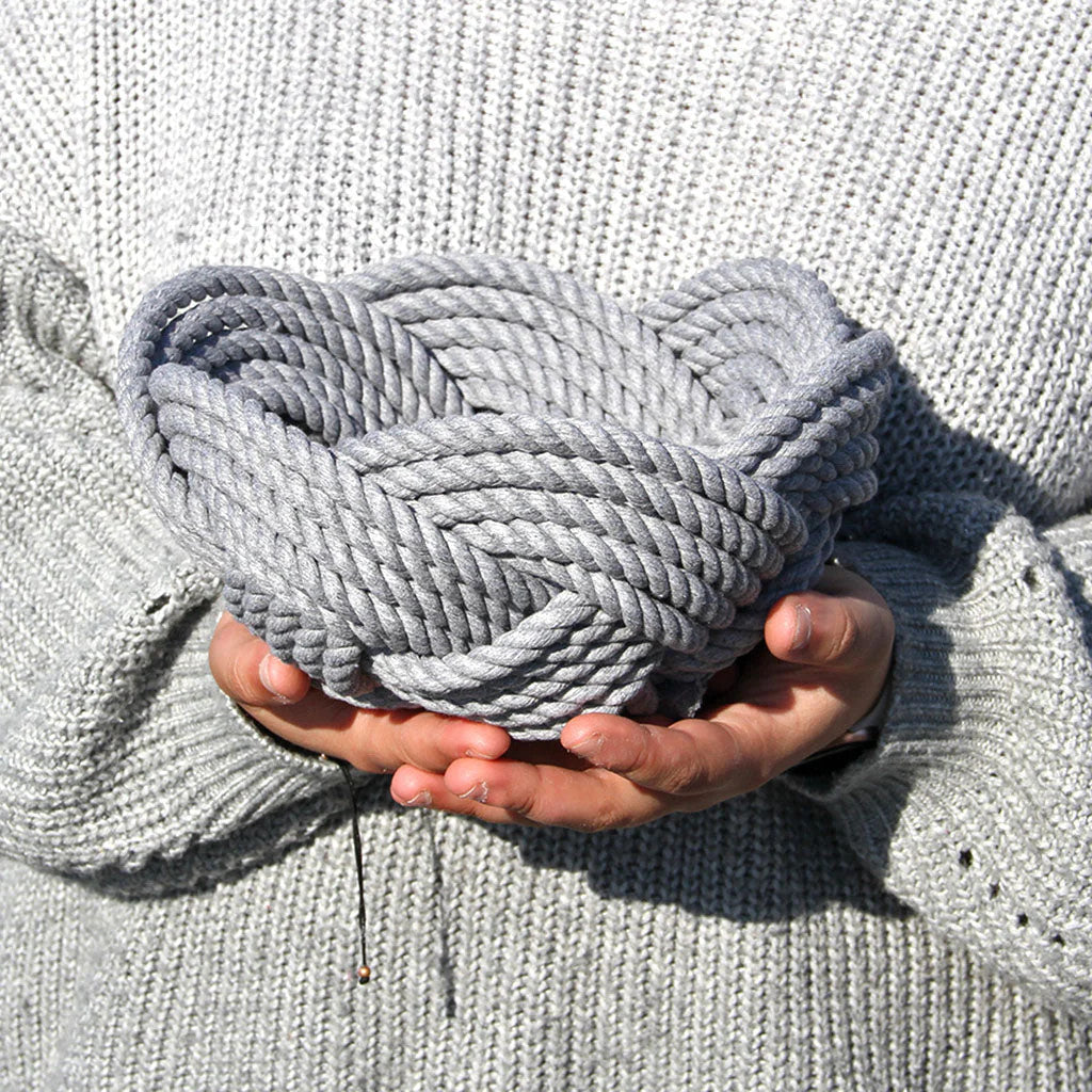 a hand woven cotton rope bowl in gray as seen in the hands of someone holding it about chest high showing that it is slightly wider than two hands loosely clasped together