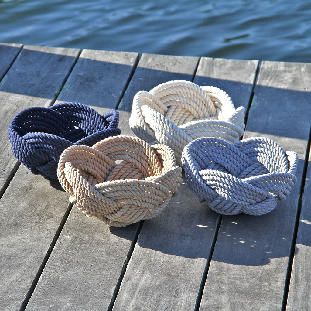a collection of all of the colors of hand woven celtic knot rope bowls on a dock: navy, tan, white, and gray