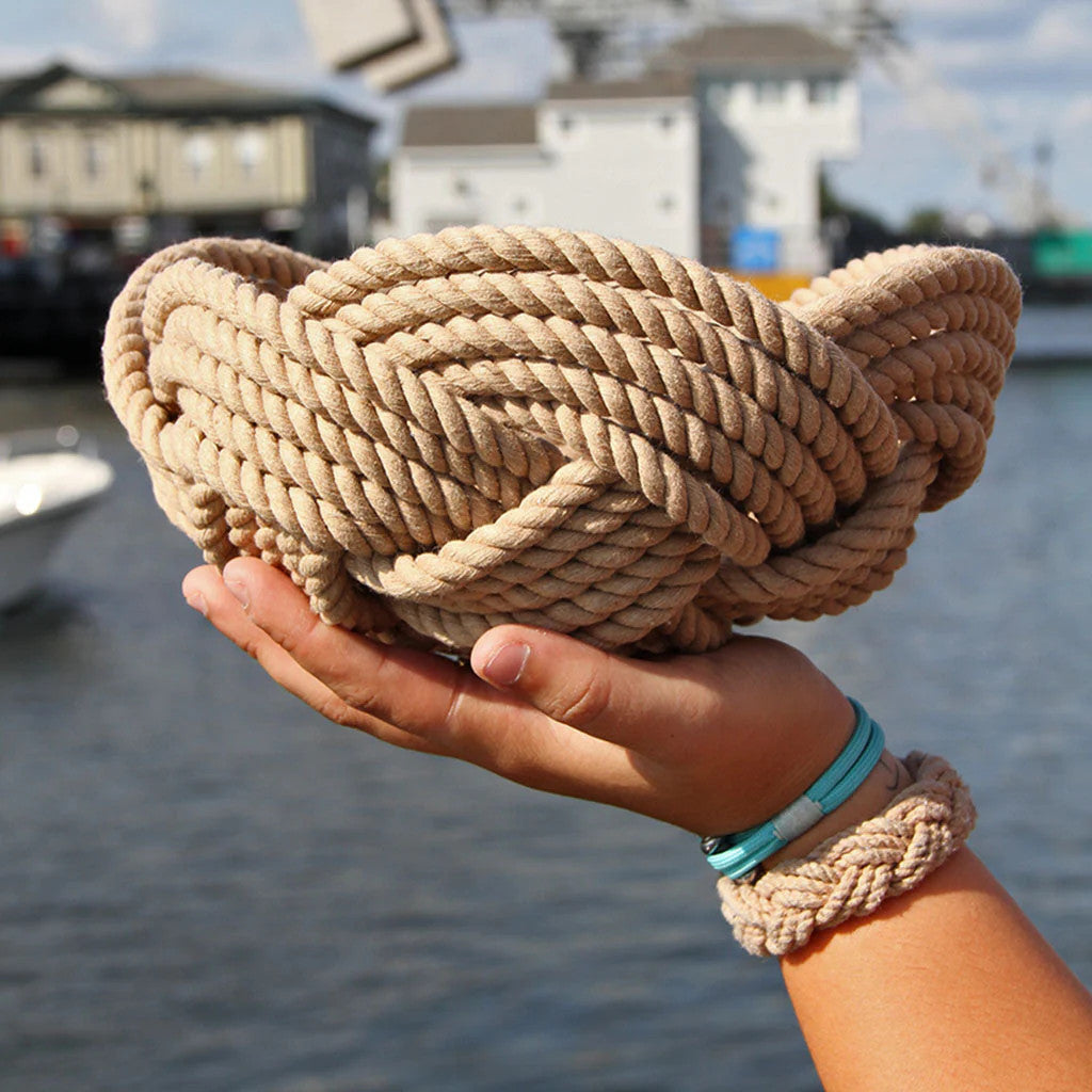 a hand woven cotton rope bowl in tan as seen in profile being held up by one single hand showing the scale of the bowl