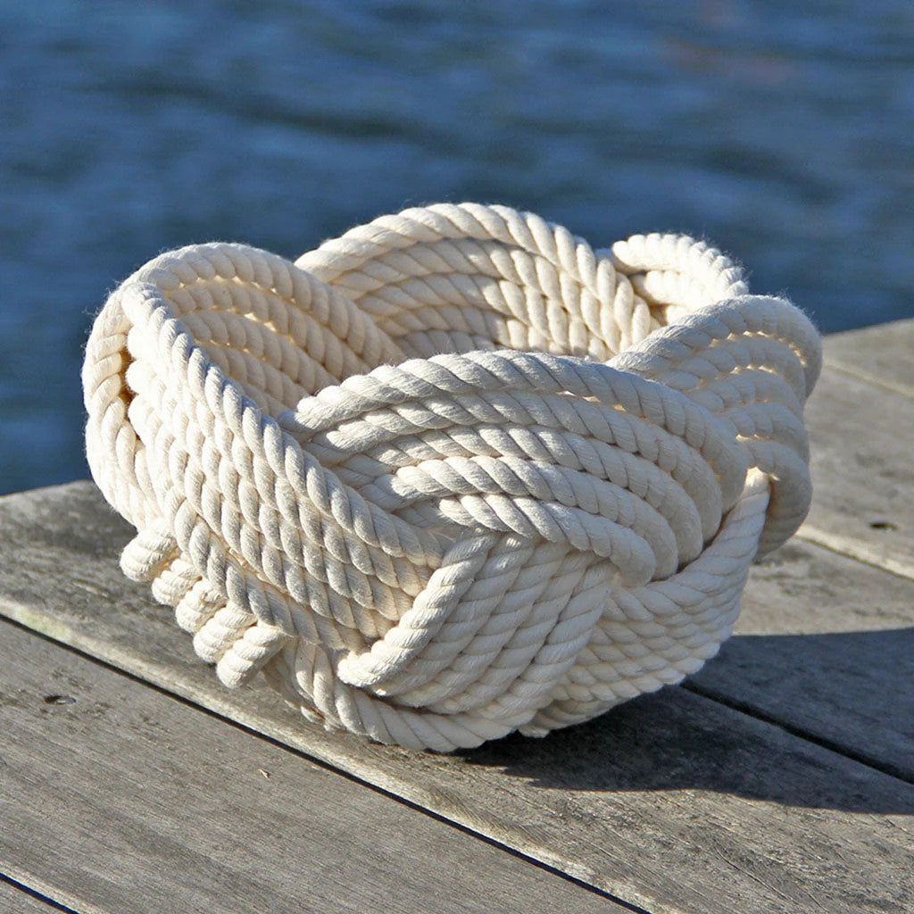 a hand woven cotton rope bowl in white resting on a dock with a view of the water