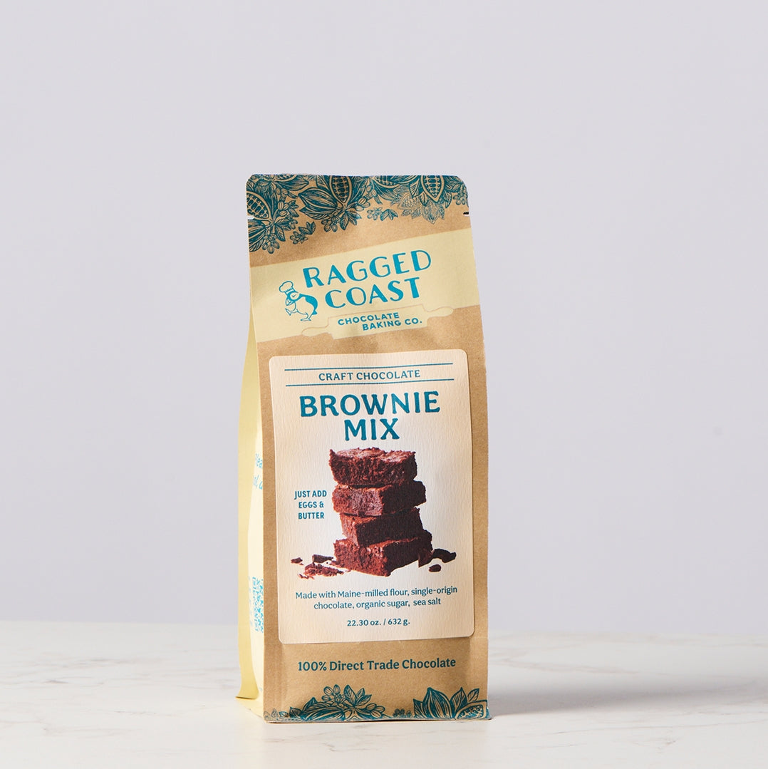 A bag of Ragged Coast Craft Chocolate Brownie Mix, featuring a kraft paper packaging with teal decorative accents and a central white label showing a chocolate brownie stack.