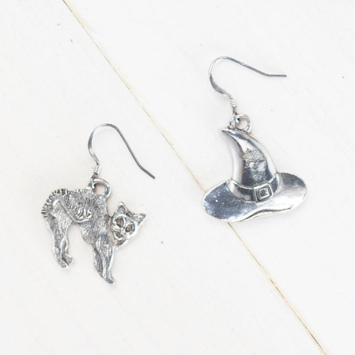 handcrafted pewter witch hat earring, featuring a small stamped star on the hat and a handcrafted pewter cat earring with detailed fur and an arched back, evoking a spooked stance, against a plain white background