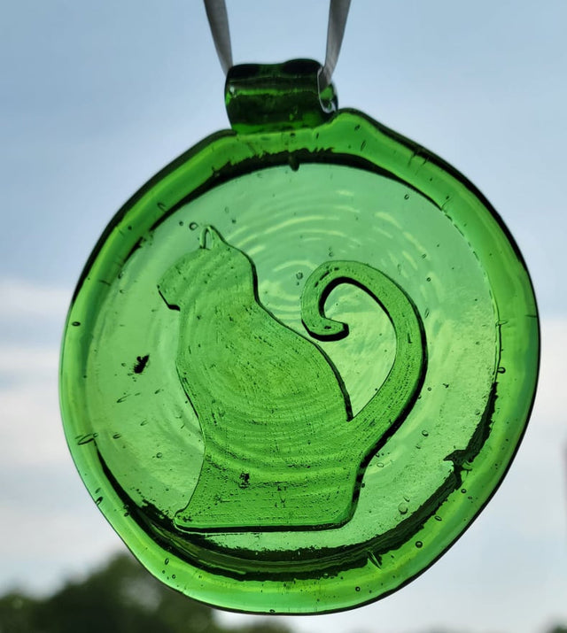Green glass suncatcher with a sitting cat design. The background is sky.