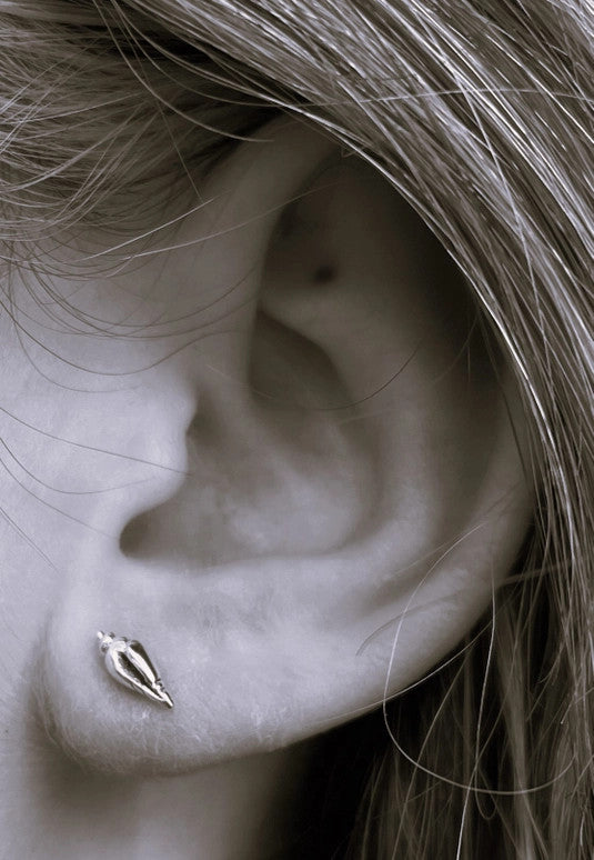 a black and white close up of a model's ear wearing the conch shell earrings