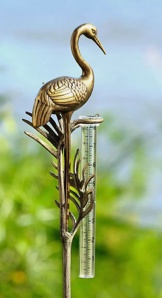 detail view of the crane rain gauge in a garden, featuring the elegant details of the crane, sculpted fronds, and clear rain gauge with markings to measure rainfall