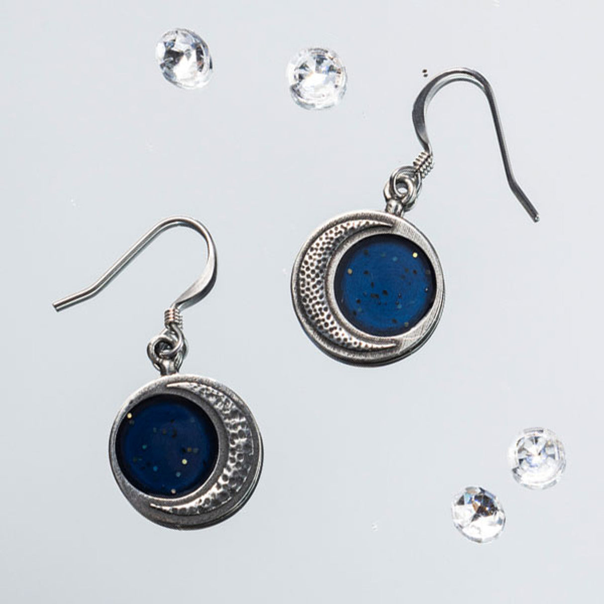 Handcrafted silver Crescent Moon Earrings featuring a stippled surface resembling moon craters, with a sparkling blue inner section, showcasing celestial beauty
