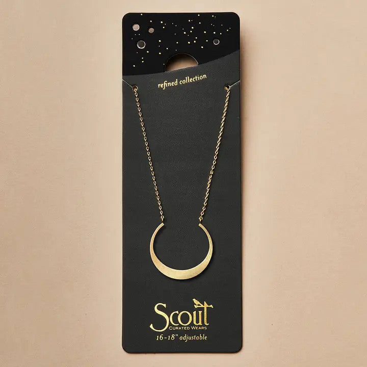 A gold necklace with a crescent moon pendant on a black card that it is packaged with