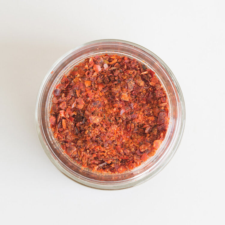 a top down view of an open jar of magic salt revealing the warm red and pink hues of the spice blend