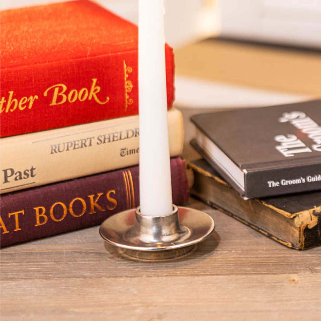 the pewter taper candle holder with a white taper candle set on a table with books