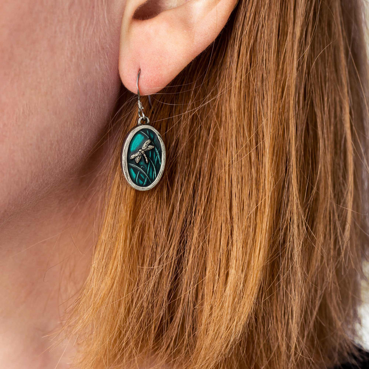 A single teal dragonfly earring worn on a model’s ear, showcasing its delicate design and elegance.