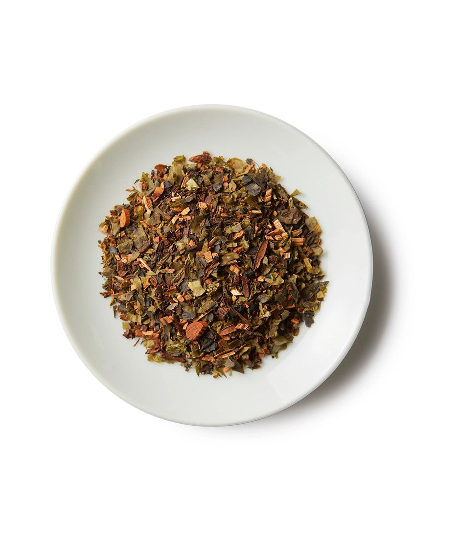 a small white round dish containing a mound of emerald honeybush loose leaf tea showing the honeybush and seaweed ingredients