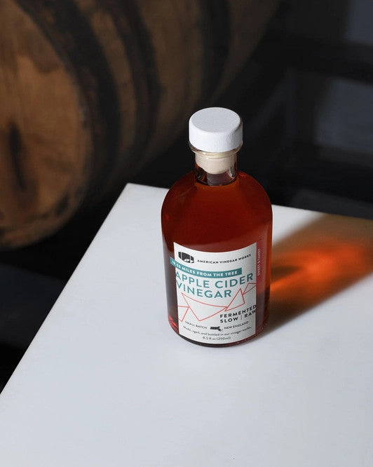 19.53 Apple Cider vinegar bottle on a table - the sun is shining directly on the bottle casting an amber reflection in the shadow of the bottle