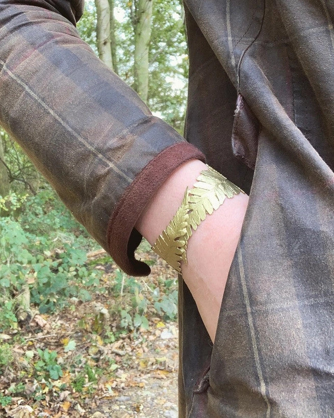 the fern cuff on a model's wrist with hand in pocket, model is wearing a green and brown plaid coat and standing in a forest
