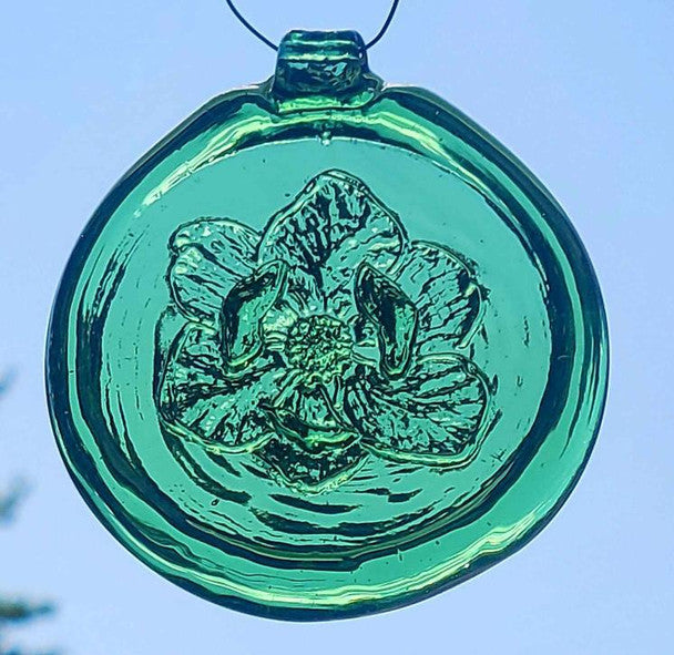 a green, round glass suncatcher with a relief image of a magnolia blossom